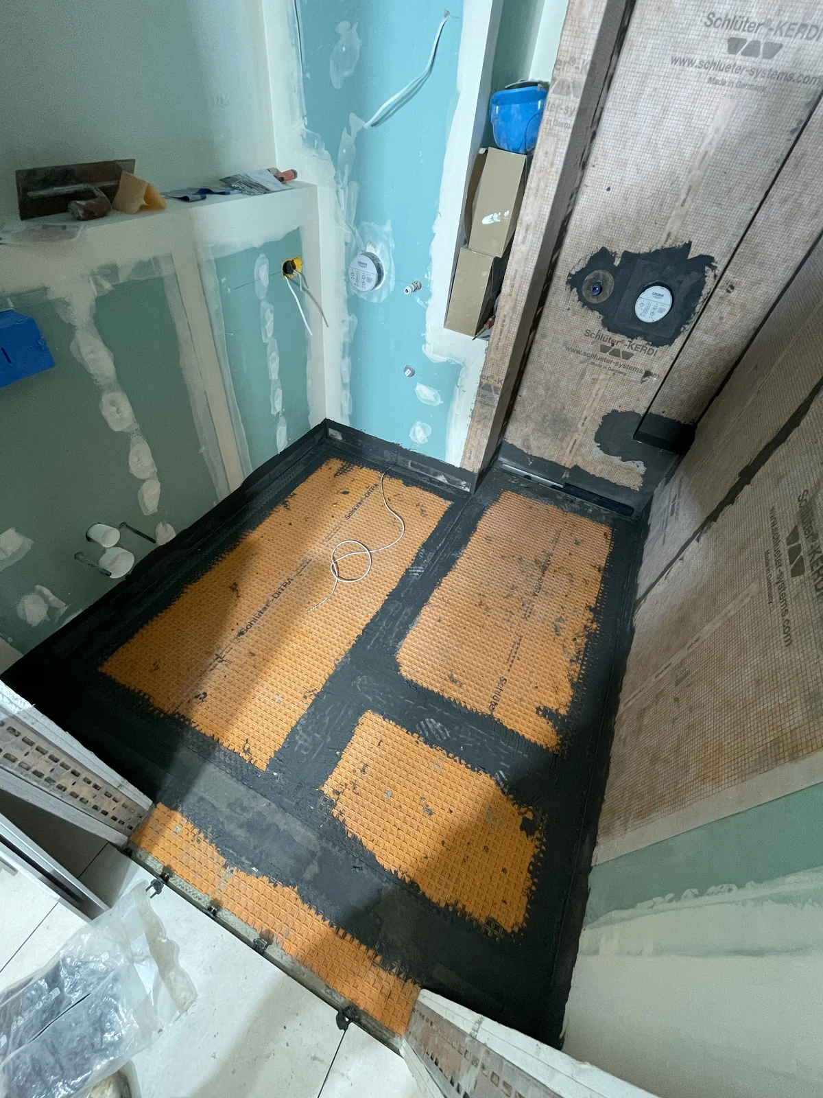 Floor membrane laid with sealed joints and edges, alongside the shower drain and concealed mixer fittings.