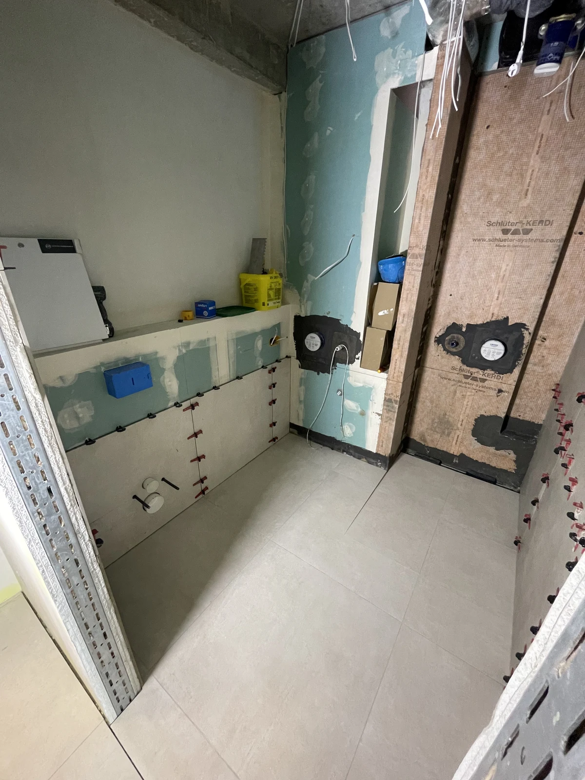 Floor tiling and wall tiling under way, with the recessed storage spaces taking shape.