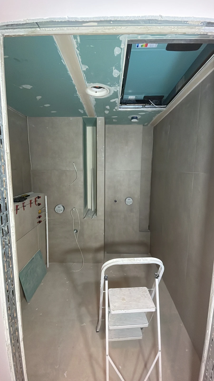 Ceiling boarding fitted around the ventilation opening, as the wall tiling continues.