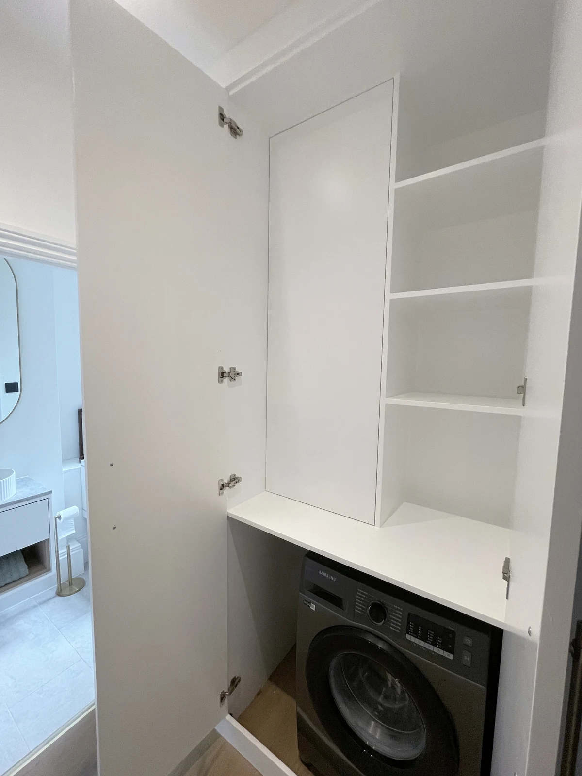 Open laundry cabinet concealing a washing machine beneath fitted shelving
