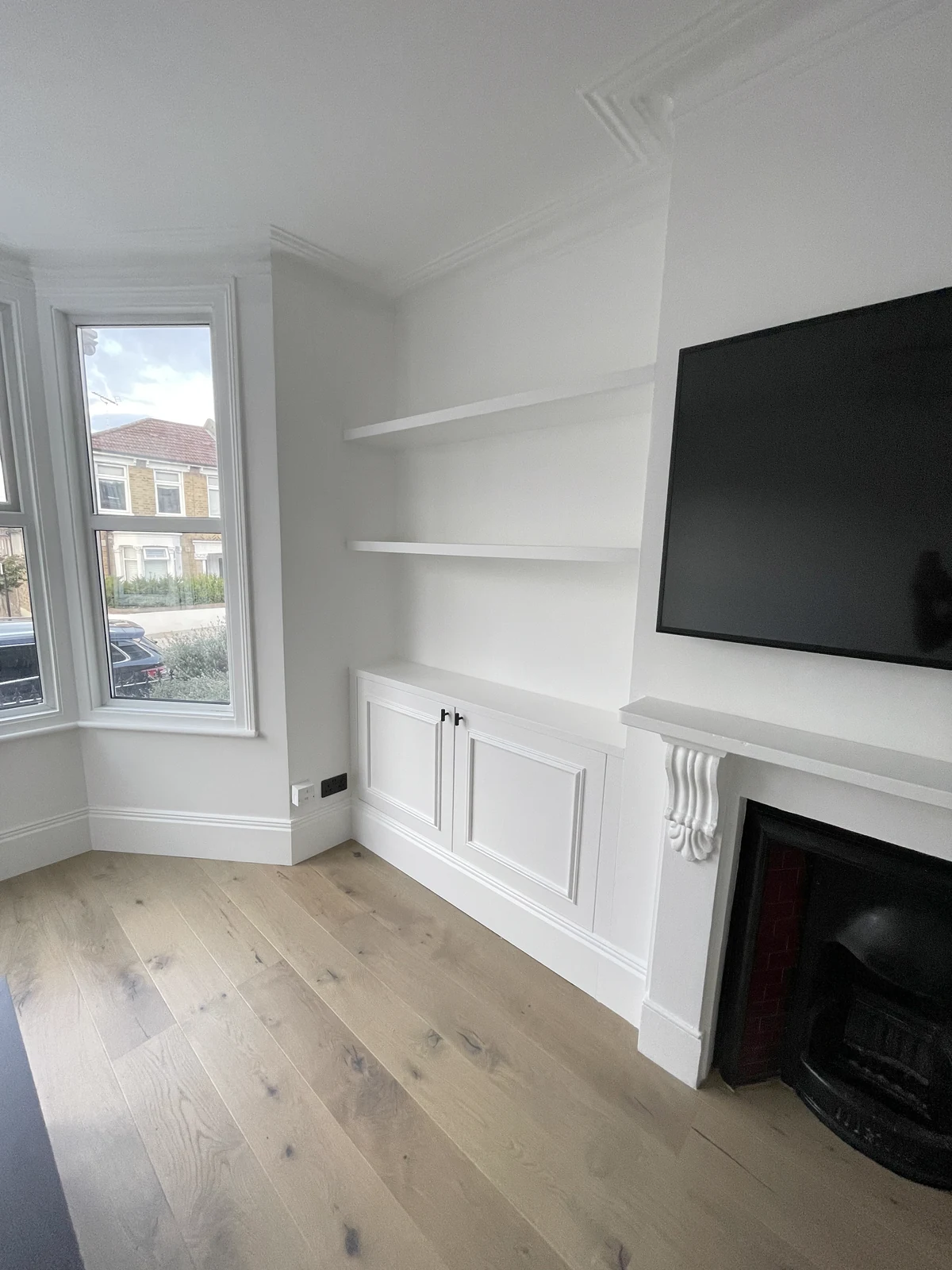 White floating shelves and panelled base cupboards beside the living-room window