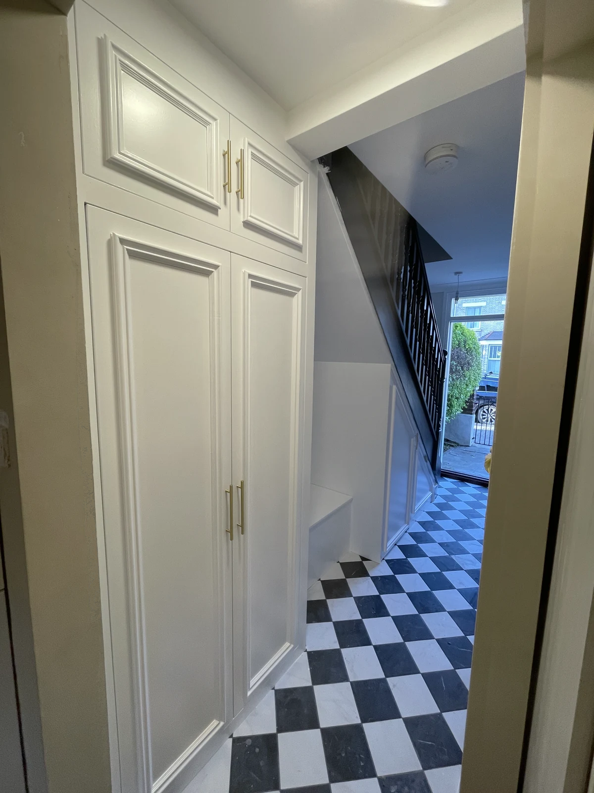 Bespoke hallway cupboards with panelled doors beside the decorated staircase.