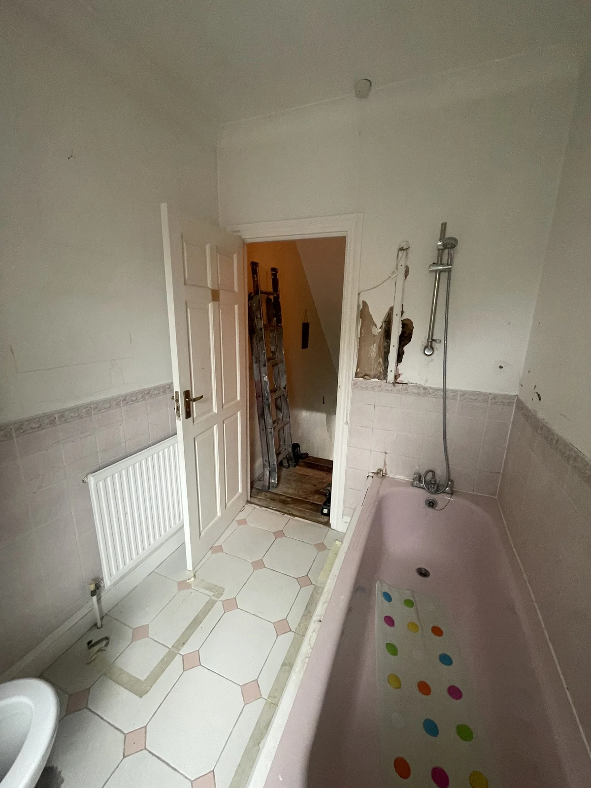 Original bathroom viewed towards the doorway, with the pink bath and earlier wall finishes.