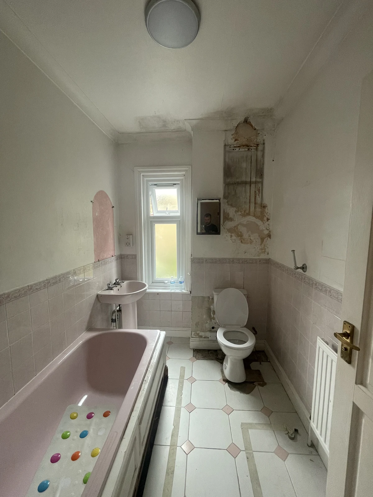 The original bathroom layout with bath, basin, toilet and patterned floor tiles.