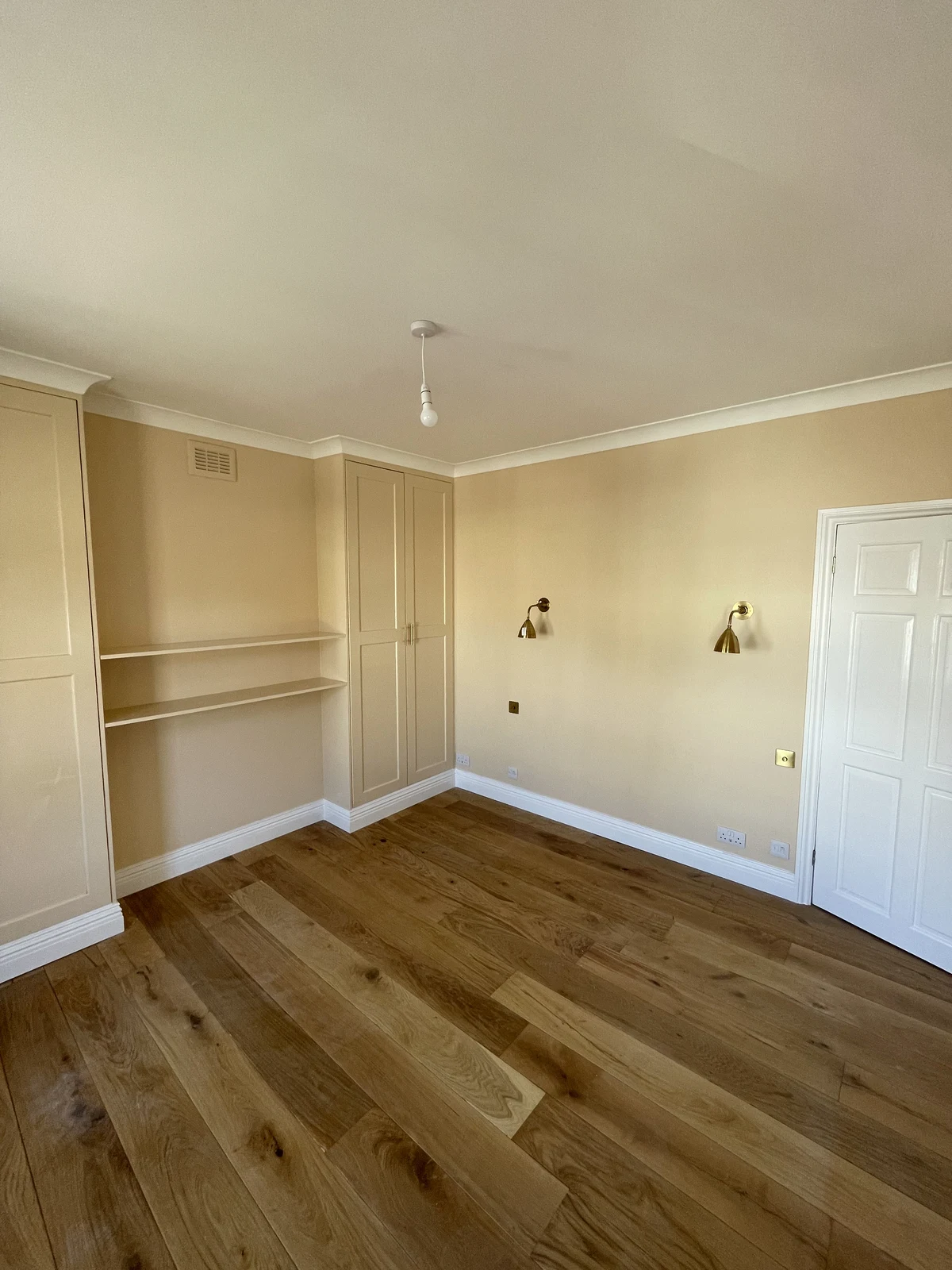 Bedroom with timber flooring, decorative wall panelling and fitted cupboards.
