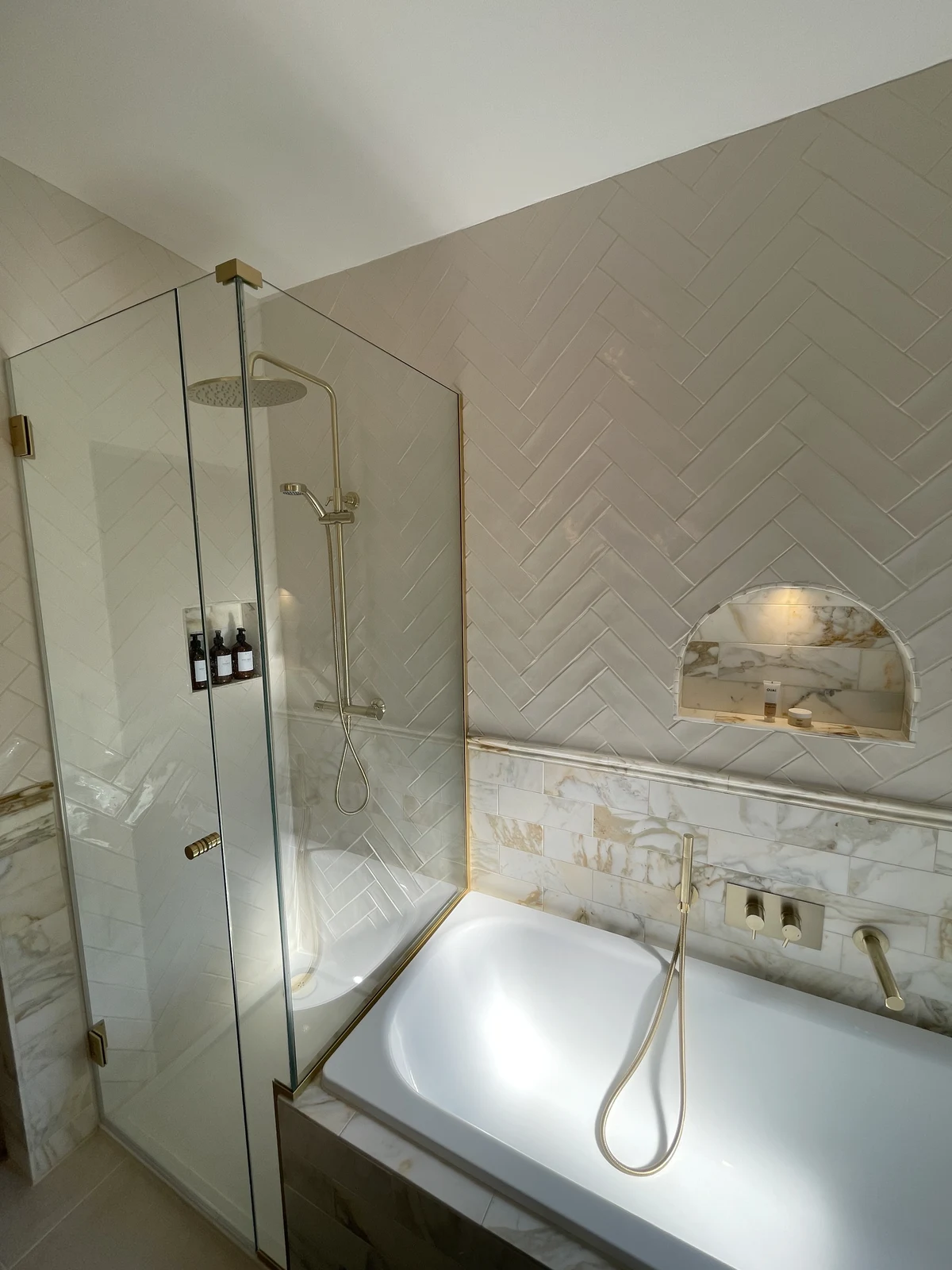 Concealed shower controls and overhead shower beside the bath and arched niche.