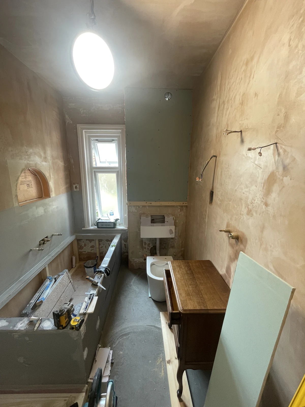 Bathroom walls prepared and replastered, with the bath and concealed toilet frame in position.