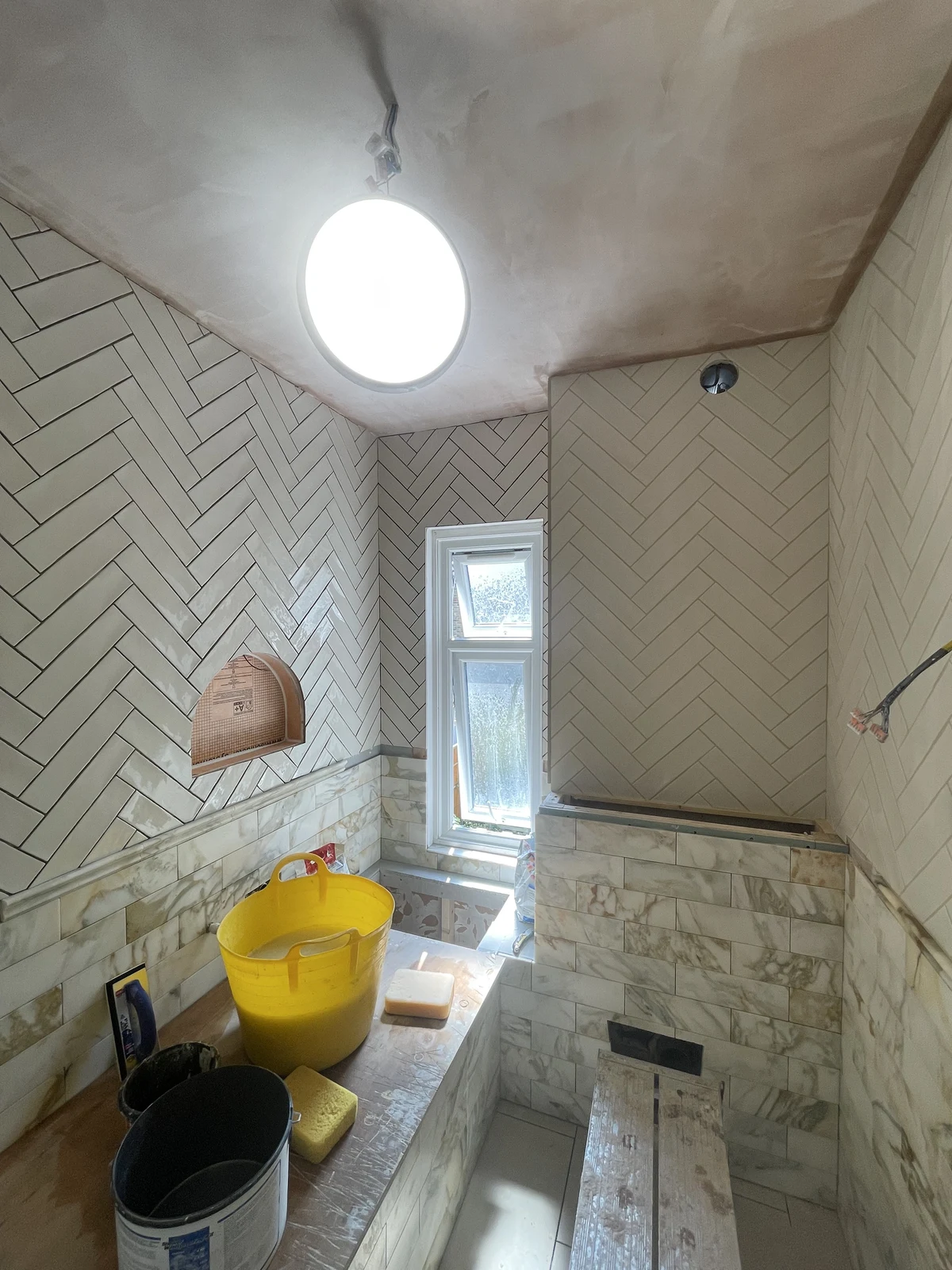 Herringbone wall tiles and marble-effect lower tiling during installation.