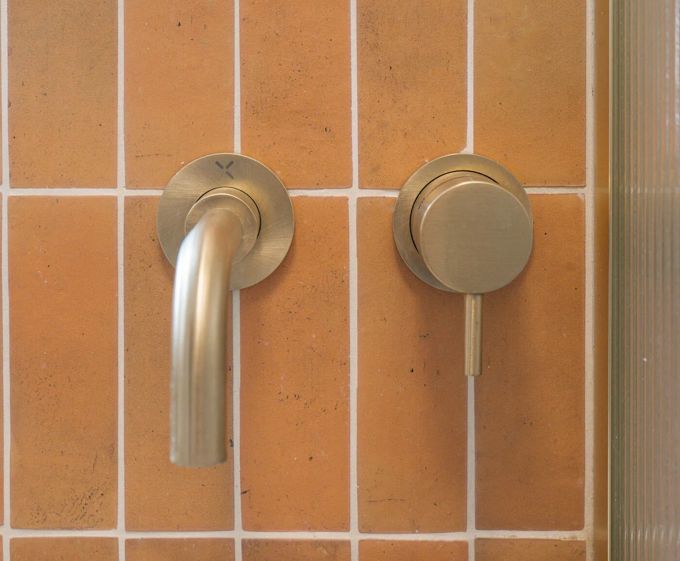 Wall-mounted basin mixer against warm orange tiles